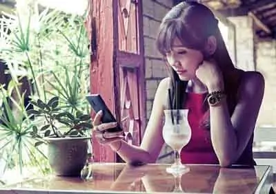 Une femme, agacée par les phrases répétitives qui l'irritent, est assise à une table, absorbée par son téléphone portable.