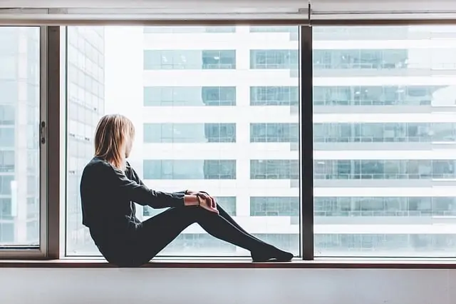 Une femme assise sur un rebord de fenêtre réfléchissant dans une ville.