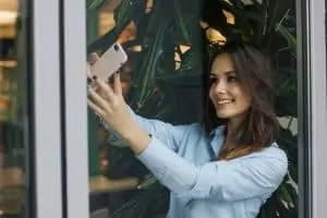 Une femme utilise Sublime-Rencontre.com pour obtenir des conseils en matière de rencontres tout en prenant une photo par une fenêtre.