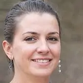 Une femme en chemise bleue souriant devant un arbre.