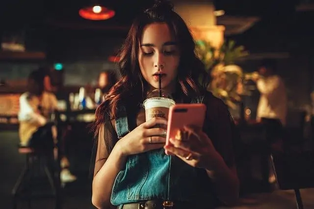 Une fille tenant un verre en regardant son téléphone, suggérant 10 questions à poser à une fille pour la charmer.